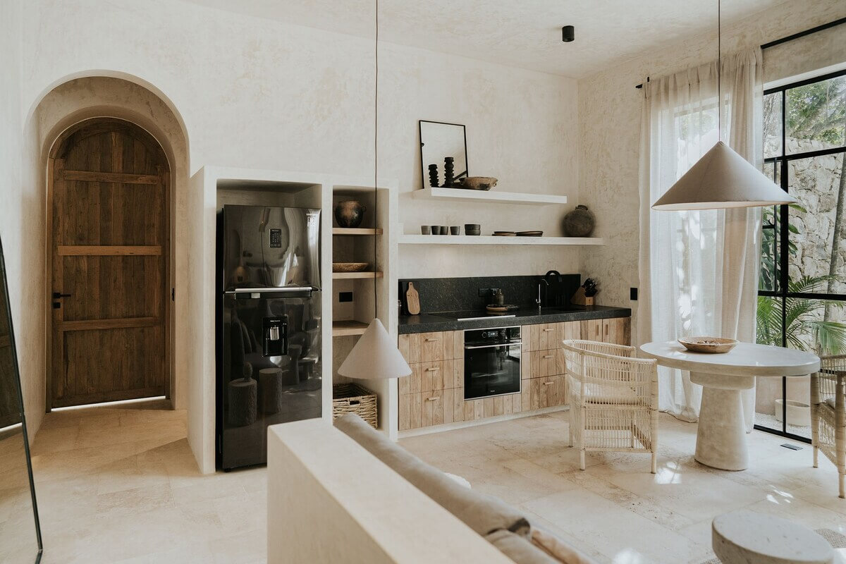 A Serene Design Apartment in Tulum 15 kitchen-living-room-shelves-round-dining-table-arched-wooden-door-nordroom